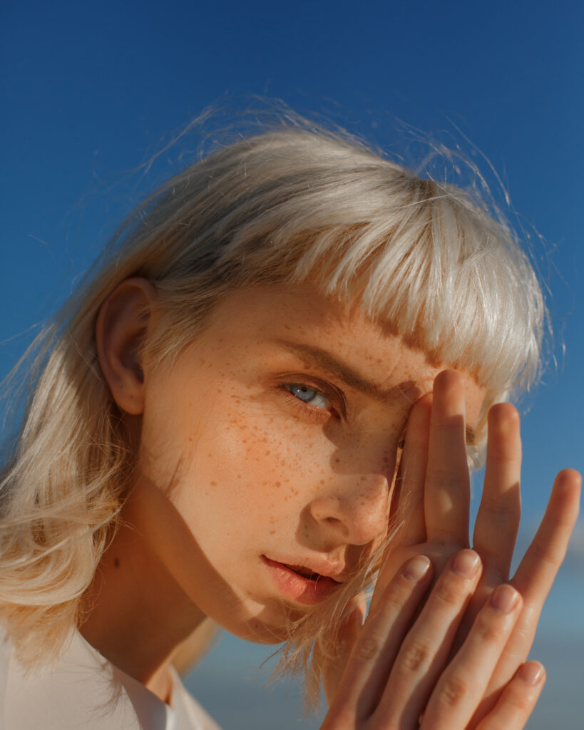 close up portrait of young blonde with blue eyes with freckles against blue sky