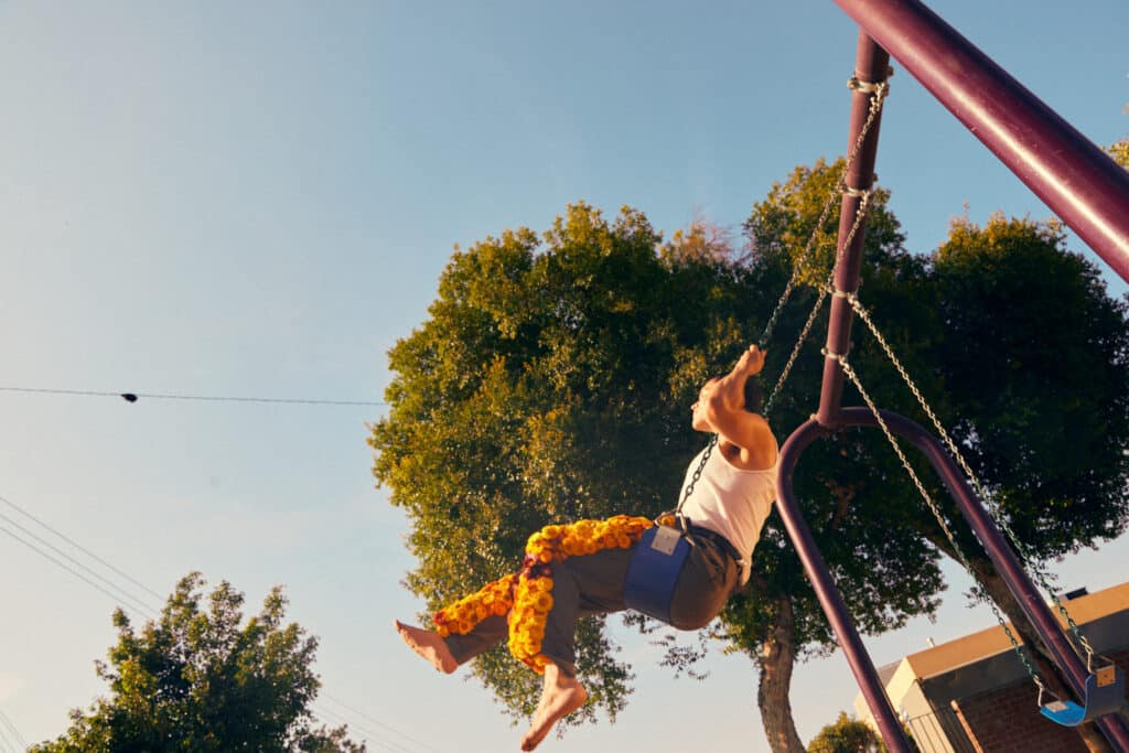 Pablo wearing pants from the flower suit and swinging on a playground swing.