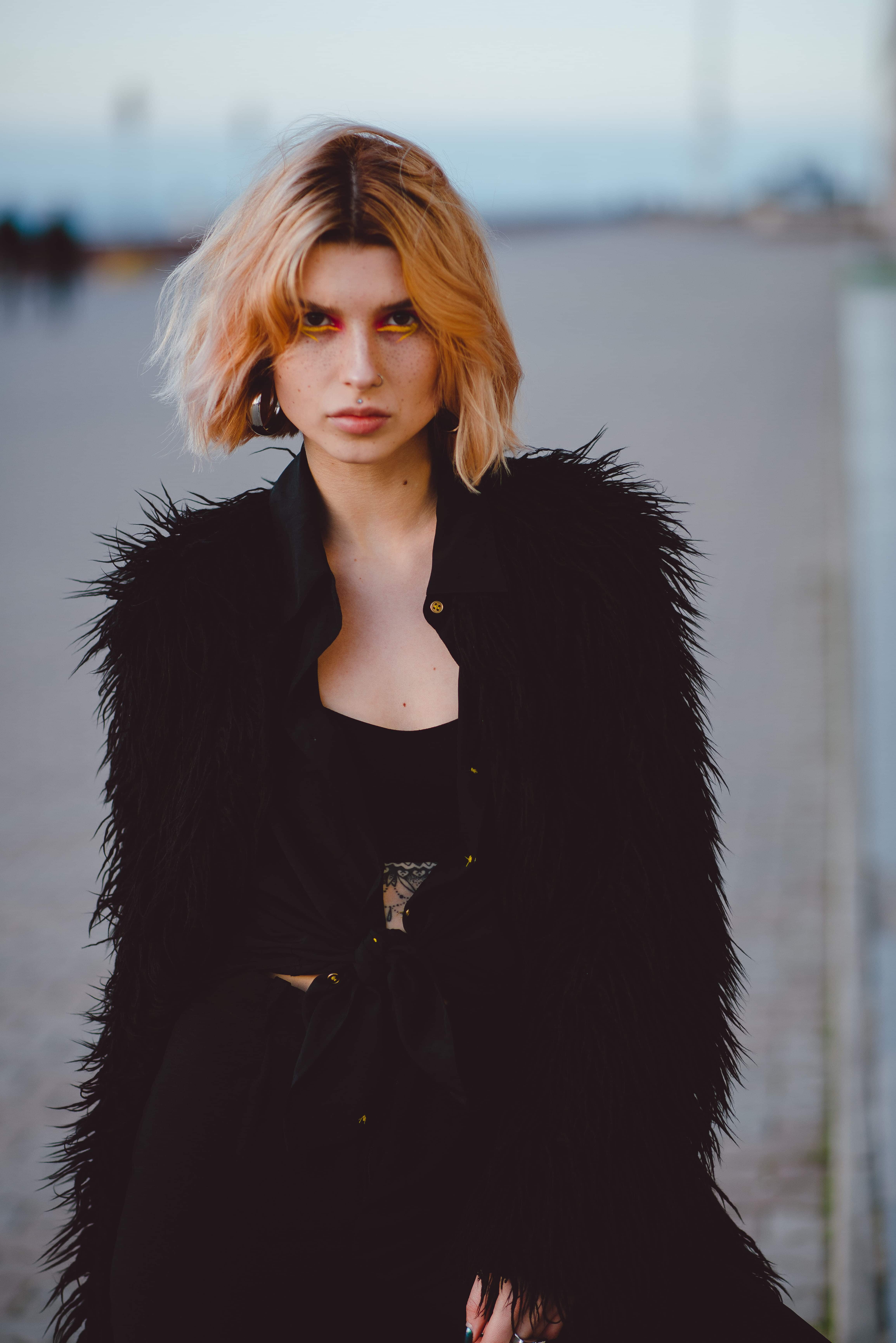 Outdoor portrait of young attractive grunge woman with colorful make up, piercing and freckles looking at the camera on the street.