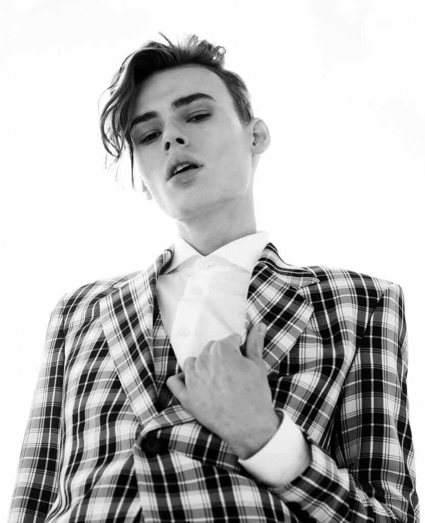 Portrait of handsome fashion male model dressed in elegant suit posing outdoor. Long haired androgynous