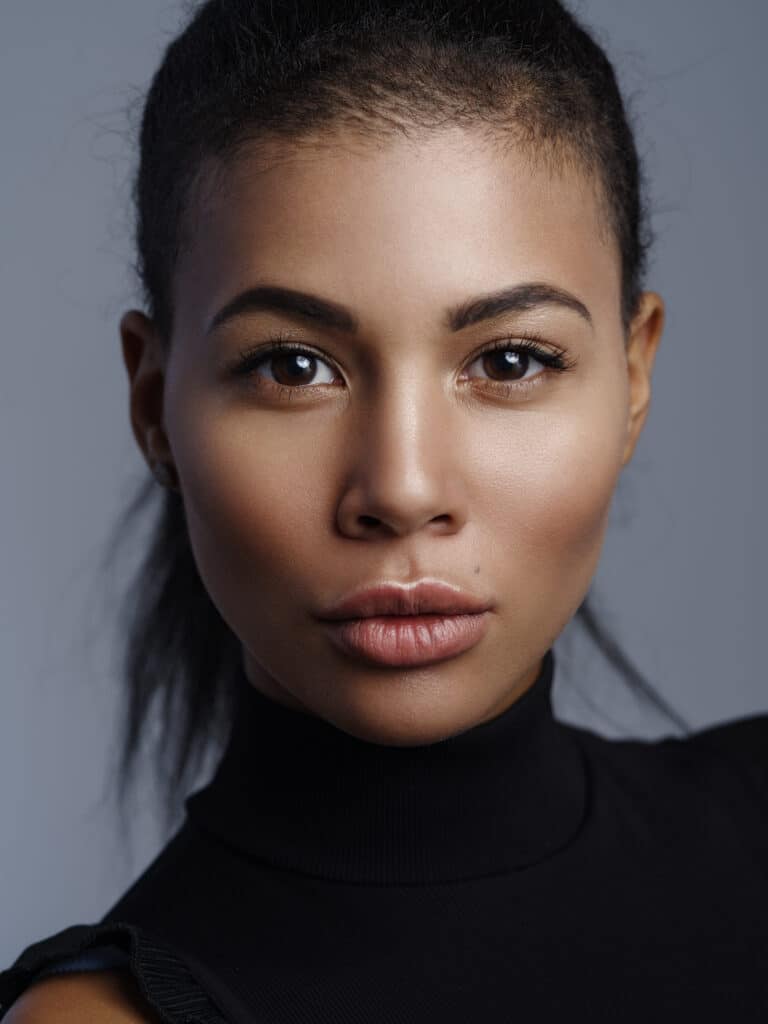 Closeup fashionable portrait of a beautiful metis young woman with perfect smooth glowing skin, full lips and collected hair. Studio shoot of an african american female model with nude makeup