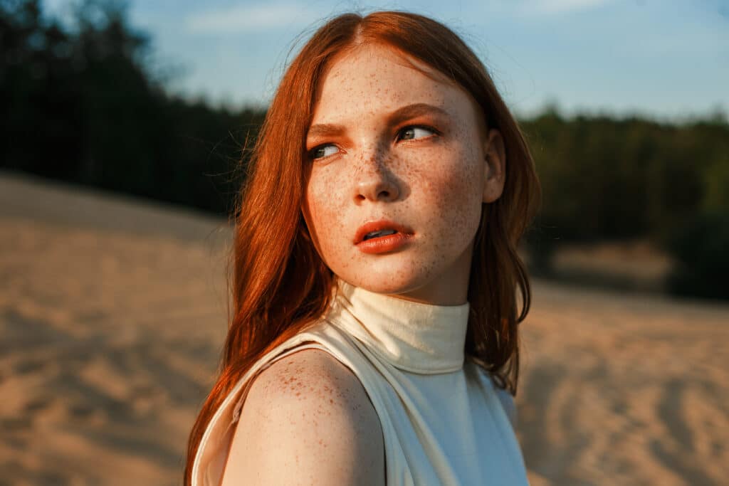 Redhead model with freckles standing in nature at sunset and looking away