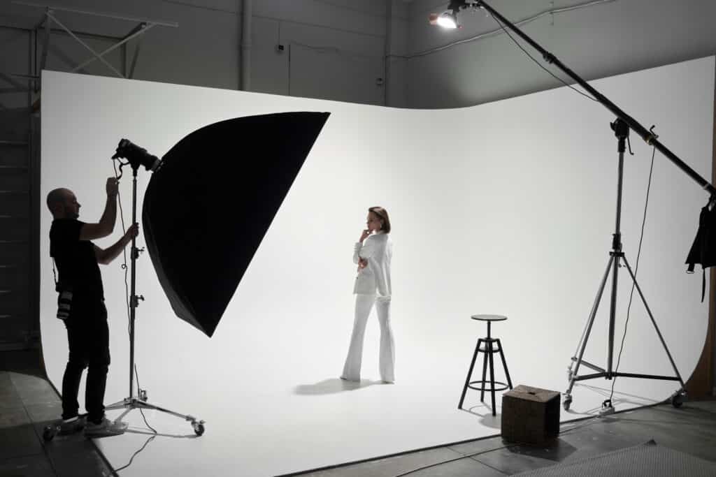 Modefotografie in einem Fotostudio. Ein professioneller männlicher Fotograf fotografiert ein schönes Frauenmodell vor der Kamera, hinter der Bühne.
