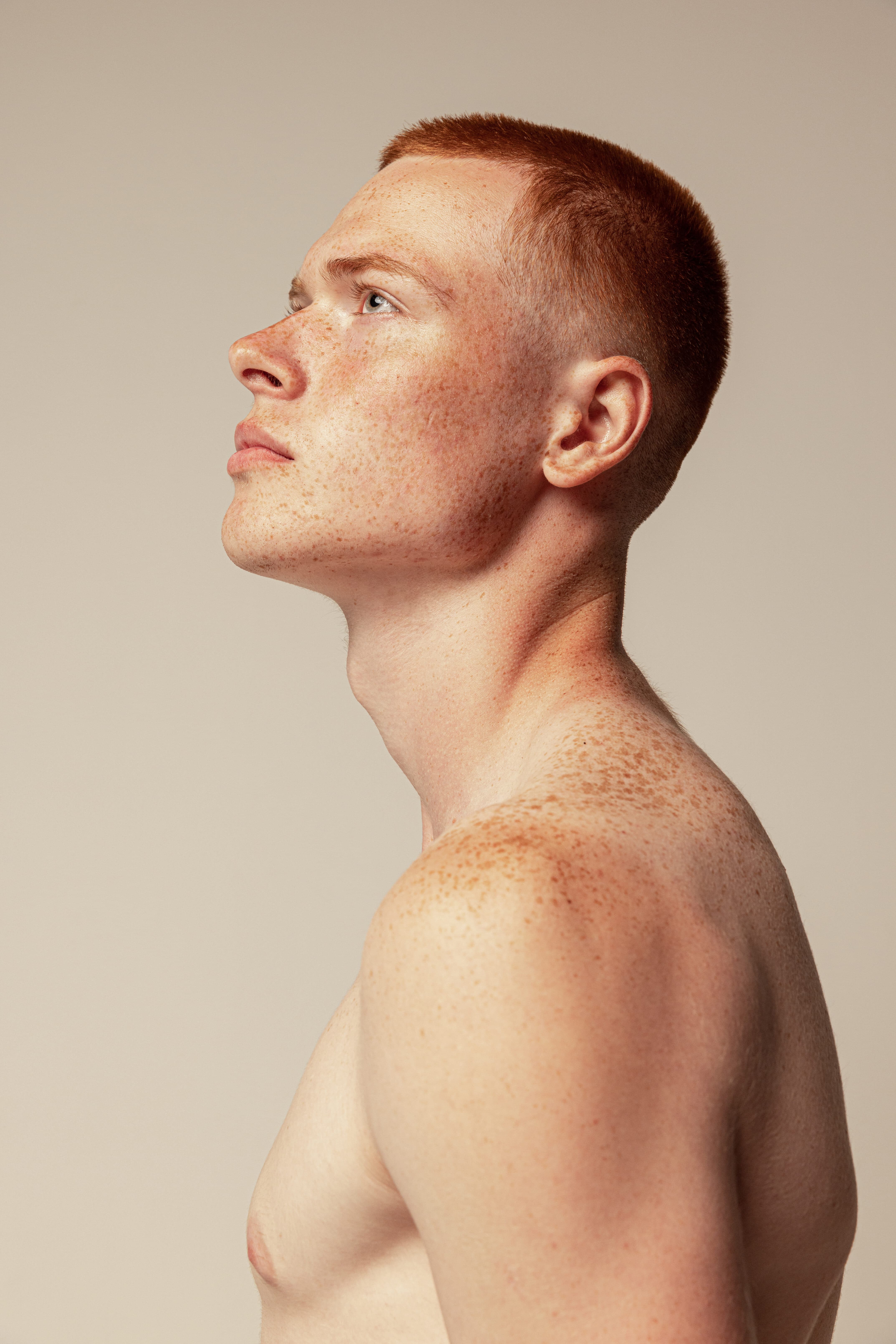 Side view portrait of attractive young red haired man with muscular body shape posing isolated over beige studio background