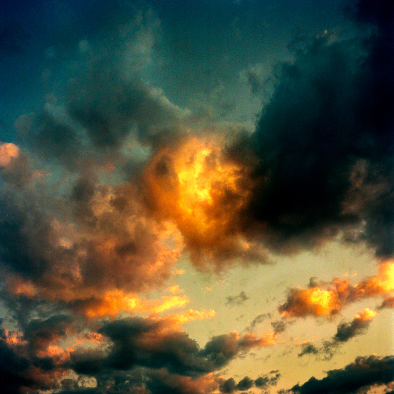 A dramatic sky features dark, ominous clouds contrasted by patches of vibrant orange and yellow light. The overall effect creates a sense of both foreboding and beauty.