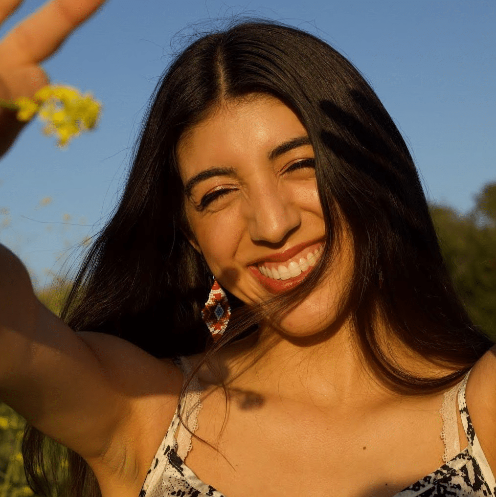 Foto de Brittany Bravo segurando uma flor silvestre sob o sol.