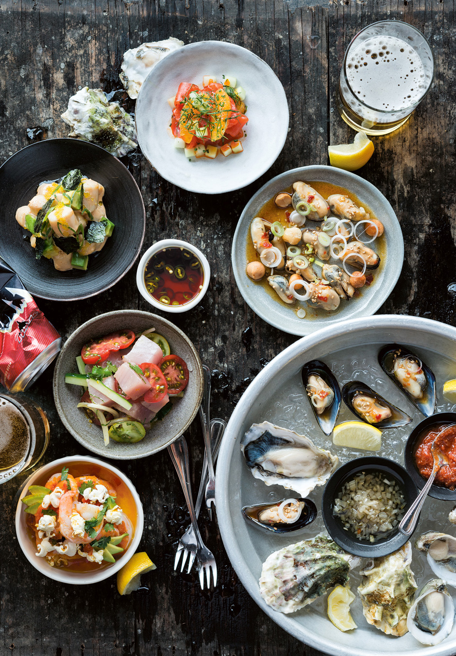 Luftaufnahme von verschiedenen Meeresfrüchtegerichten: Austern, Muscheln und Ceviches, dazu gibt's Dips und Bier. Foto von Evan Sung