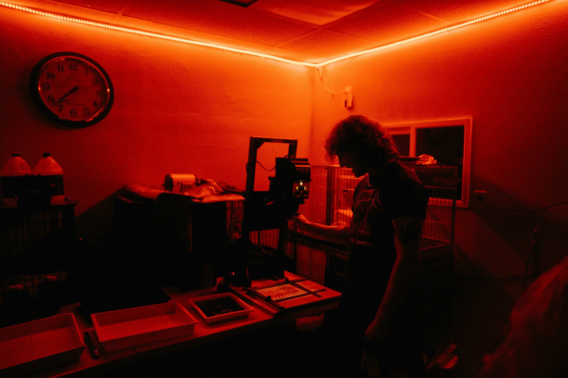 Ein Fotograf arbeitet in einer rot beleuchteten Dunkelkammer mit einem Vergrößerungsgerät und entwickelt Abzüge.