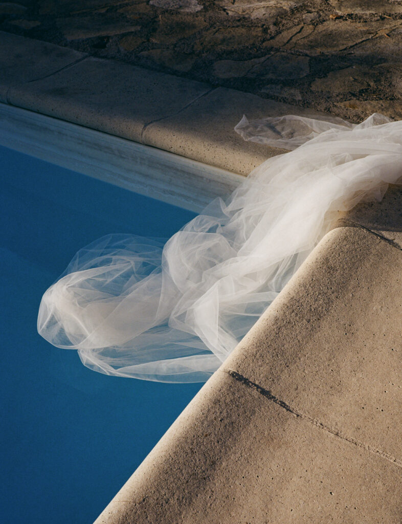 Um véu de tecido branco flutuando na beira de uma piscina azul. Foto de Nick Prideaux.
