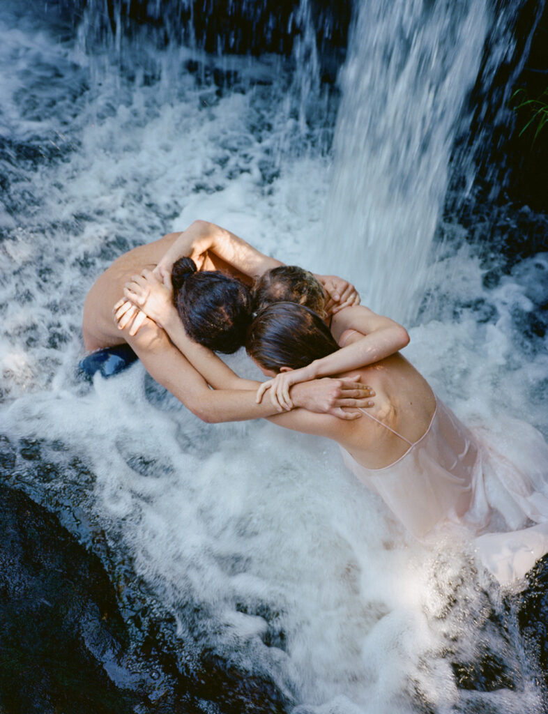 Três pessoas se abraçando em uma cachoeira turbulenta. Foto de Nick Prideaux.