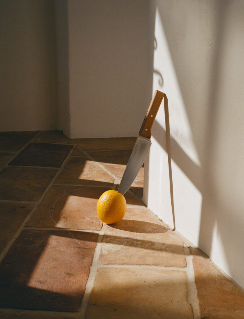 Uma faca grande encostada na parede com um único limão amarelo no chão à sua frente. Foto de Nick Prideaux.