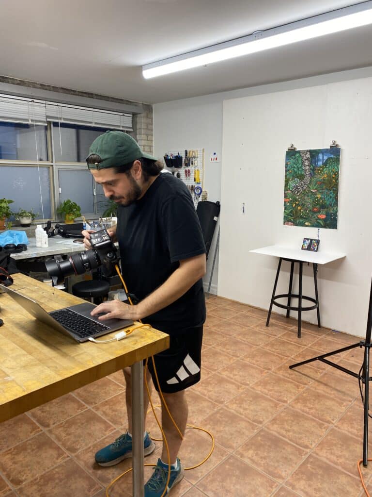 Ibrahim Abusitta verificando imagens em um laptop conectado enquanto documenta a obra de arte de Stanzie Tooth