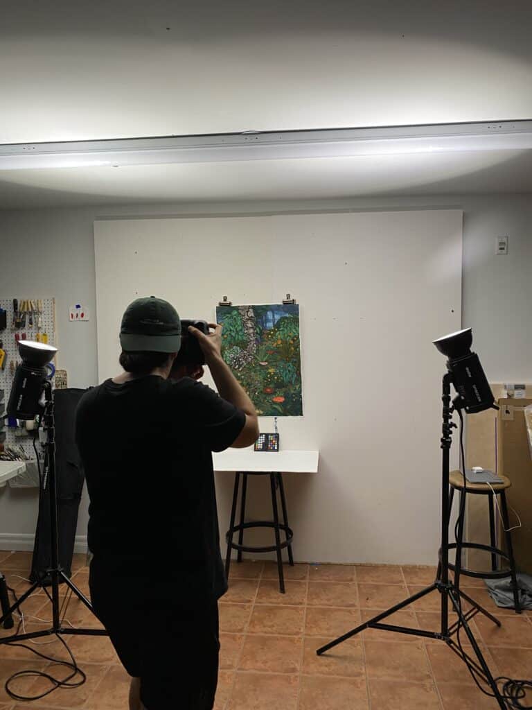 coloridas y detalladas obras de arte de Stanzie Tooth colgadas en la pared blanca mientras Ibrahim Abusitta toma fotos para documentar el trabajo