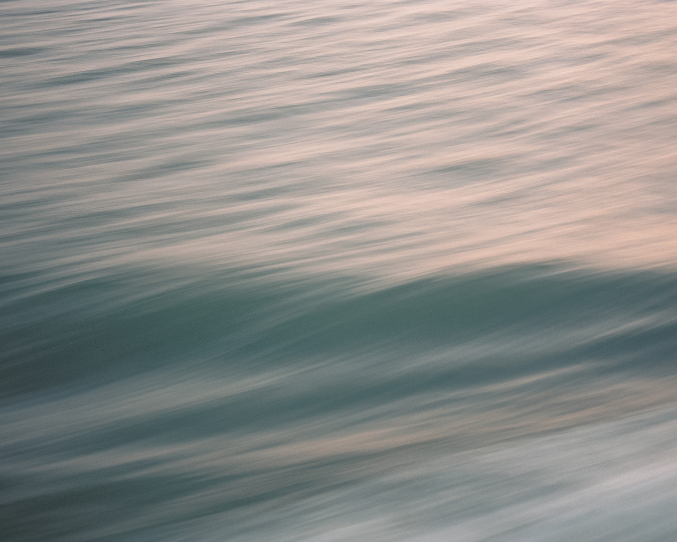 Abstract image of ocean water with motion blur, showing teal and pale pink hues. Photo by Ko Okamoto.