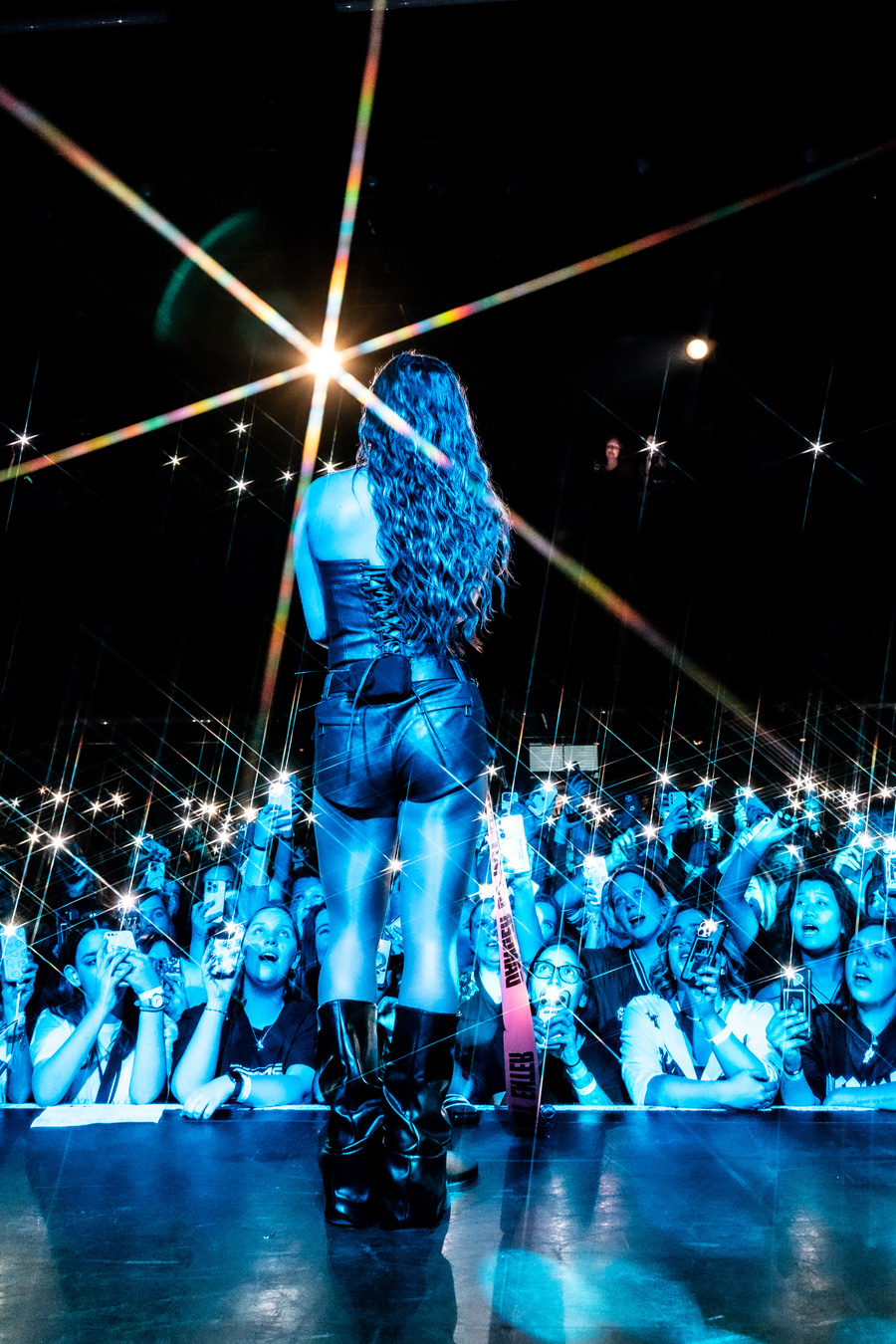 Female singer on stage facing cheering crowd with phone lights