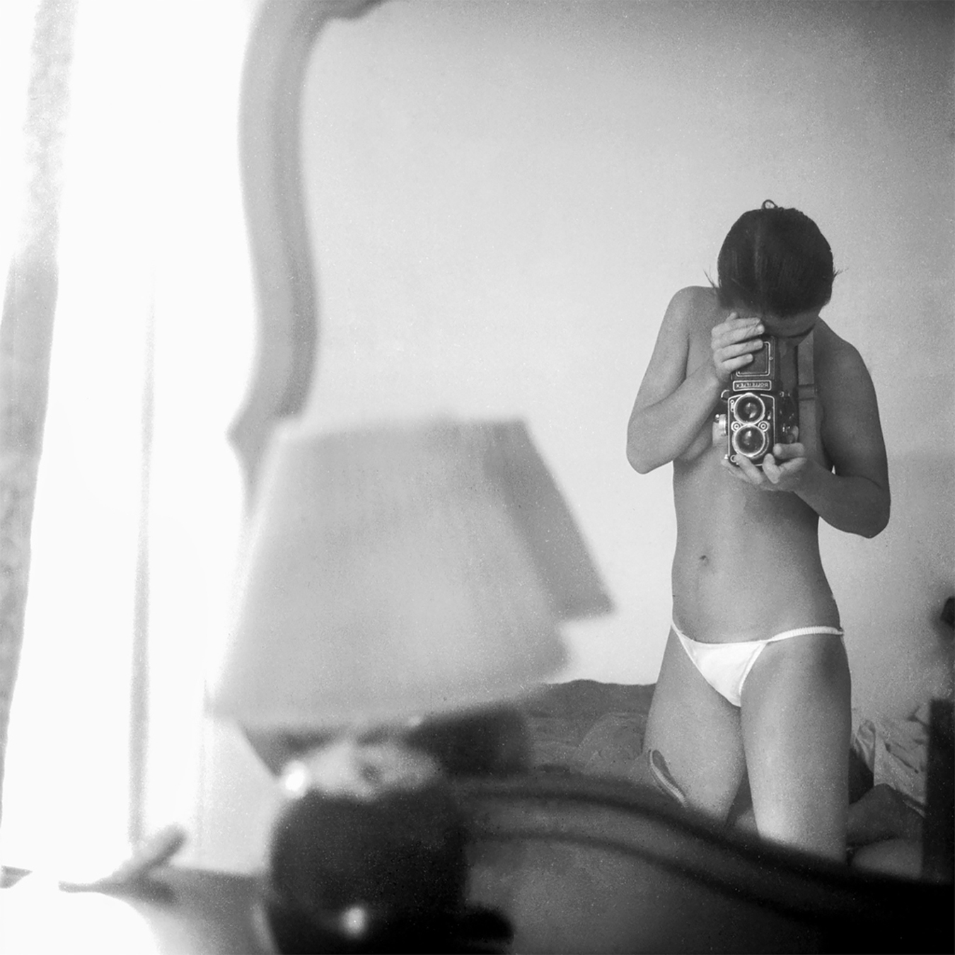 Black and white self-portrait by Marie-Laure Sorbac showing a topless woman looking down at a Rolleiflex camera.