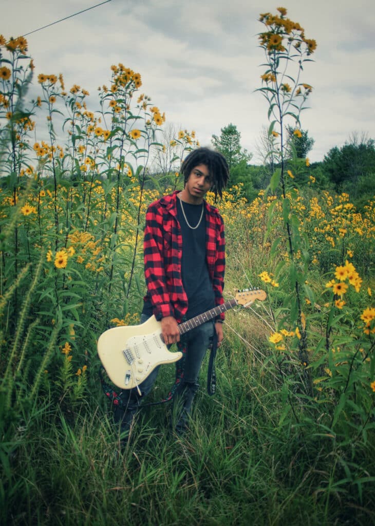 Fotografía de Naomi Bielefeldt de Colin, estudiante de último curso de secundaria, en un campo con la guitarra en la mano.