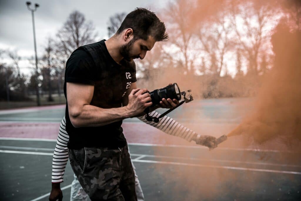 Photographer and assistant on outdoor shoot aiming camera through colored smoke