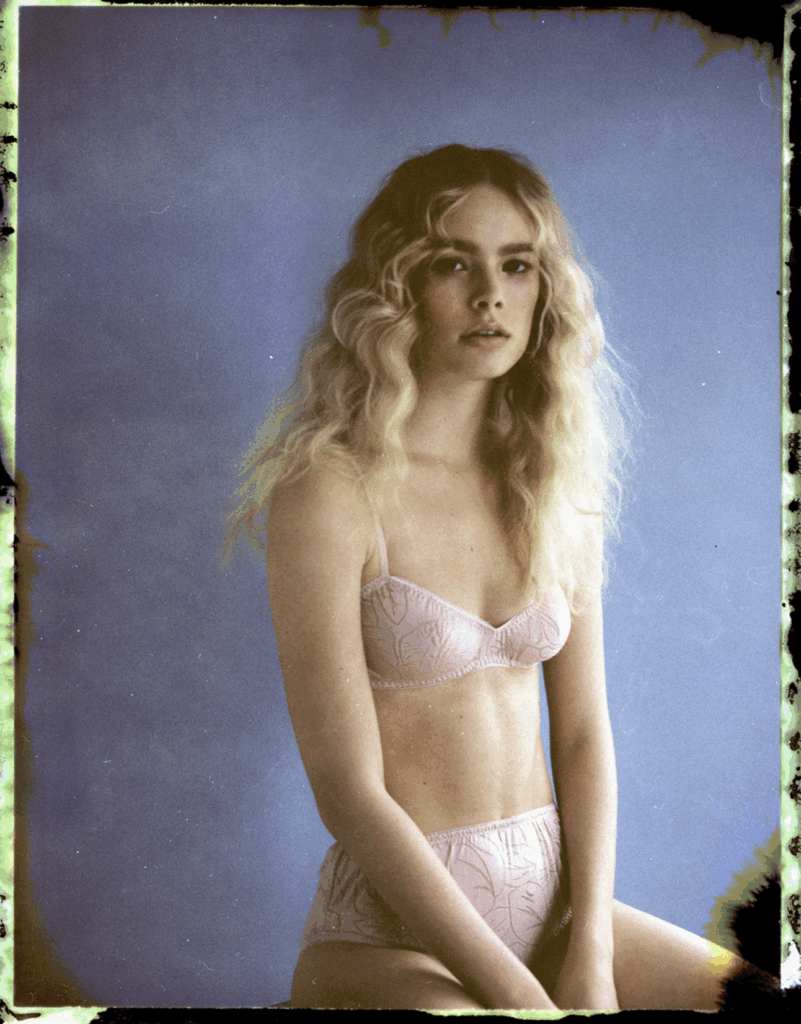 woman with blond hair posed sitting in front of a blue backdrop. Photo by Sophie Ellen