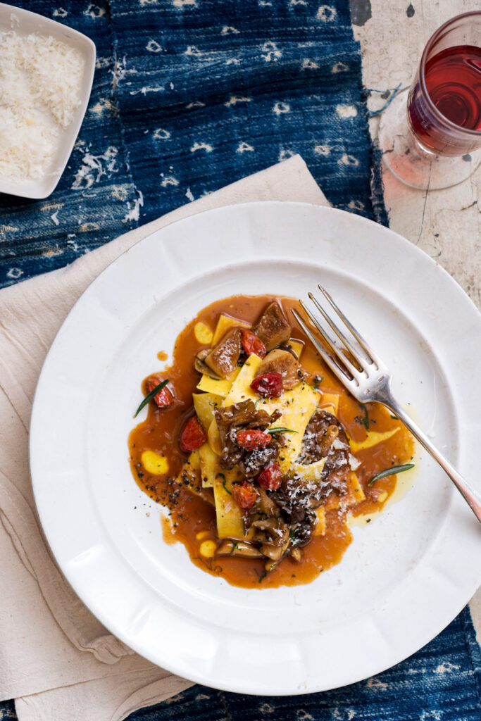 Pasta mit Pilz-Feigen-Ragout, mit Parmesan bestreut, auf einem weißen Teller serviert. Foto von Evan Sung