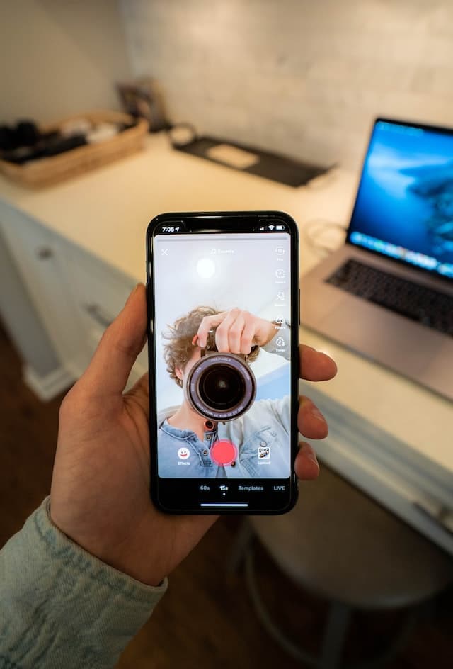 Photo d'un écran de téléphone affichant une vidéo TikTok d'un homme utilisant un reflex numérique.