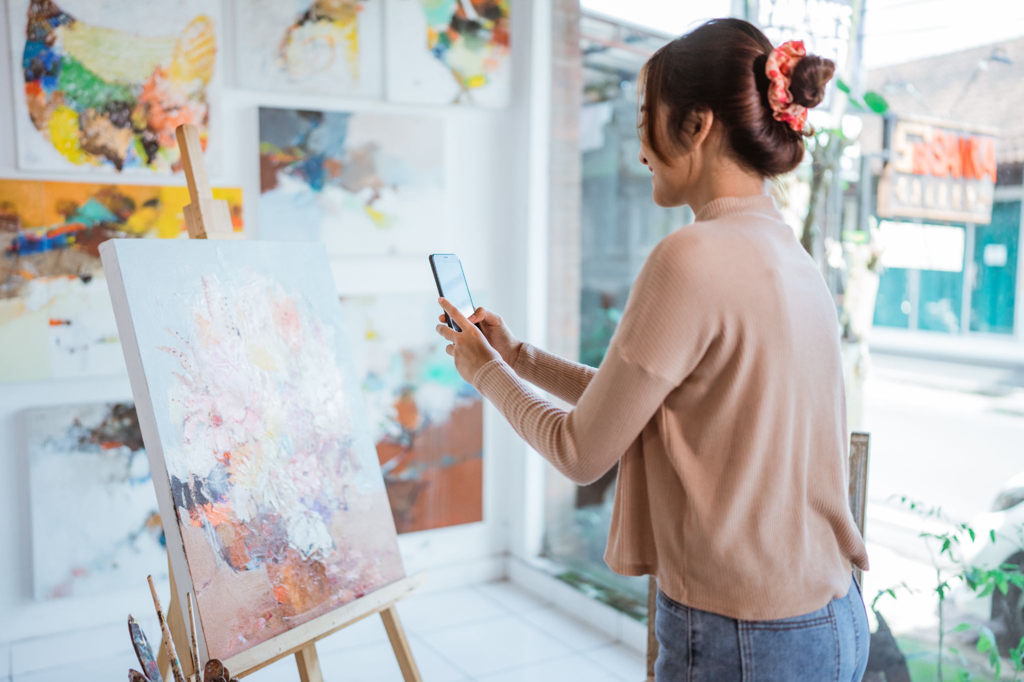 Woman photographing an abstract painting with her phone in an art gallery