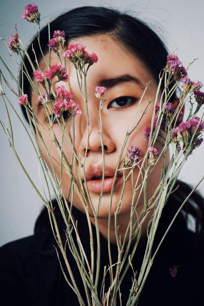 asian woman peering through a handful of dried flowers