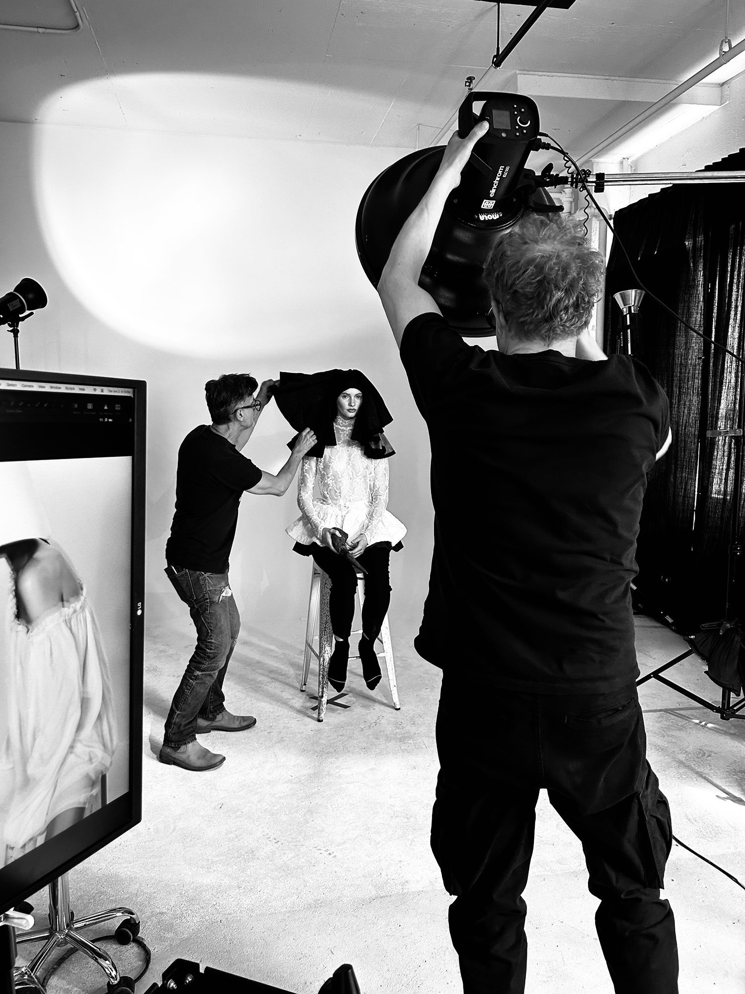 Photographer and stylist prepare a model during a fashion studio photoshoot.