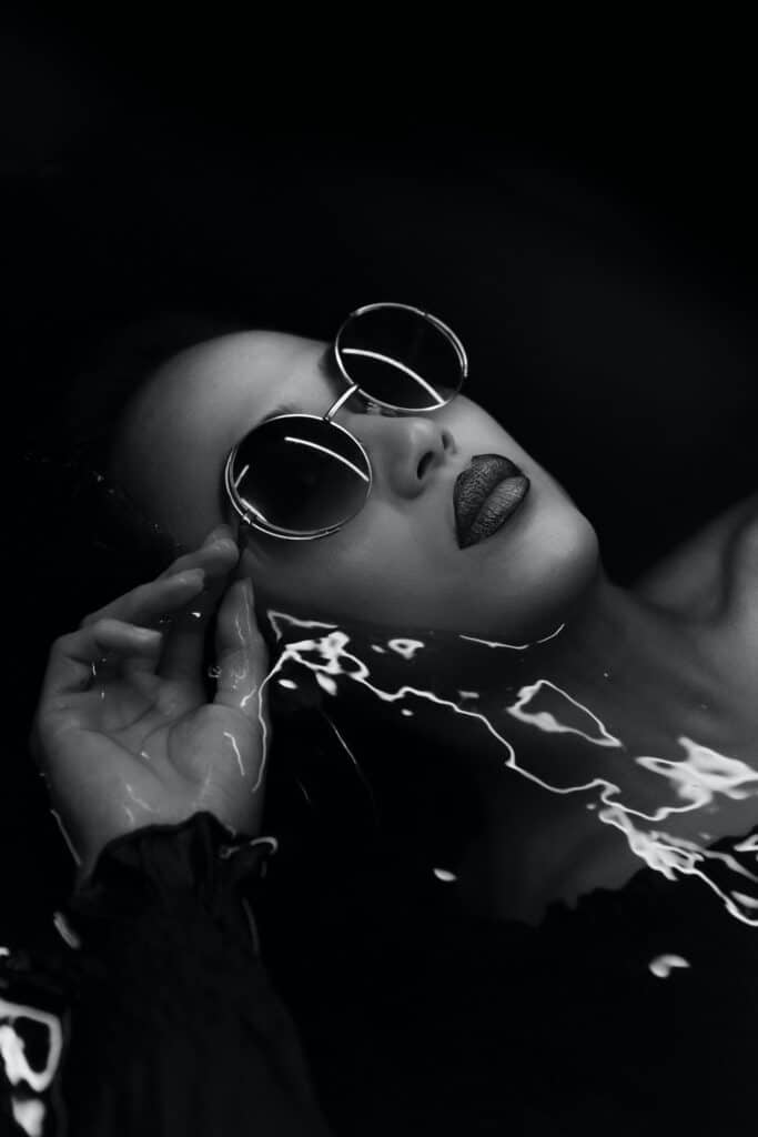 black and white photo of model wearing sunglasses laying in water