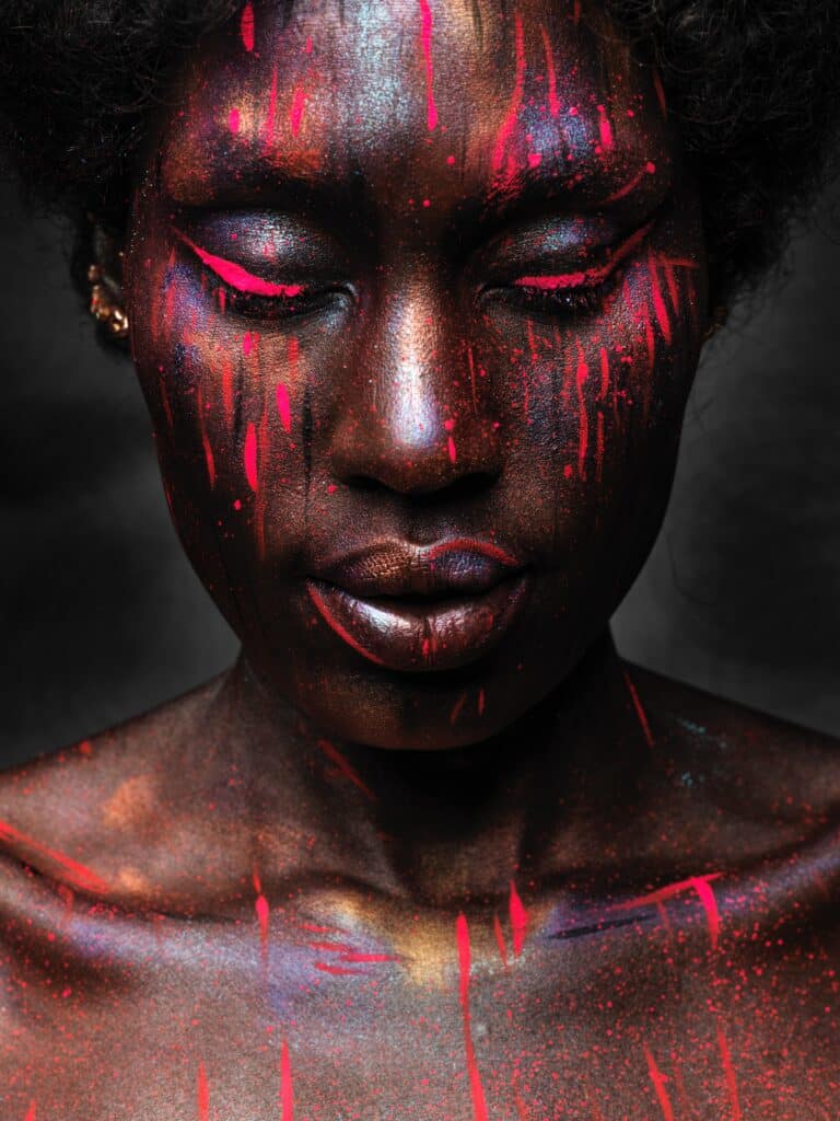 mujer negra maquillada de kuei alor con rayas rojas y azules en la cara y a lo largo de las pestañas
