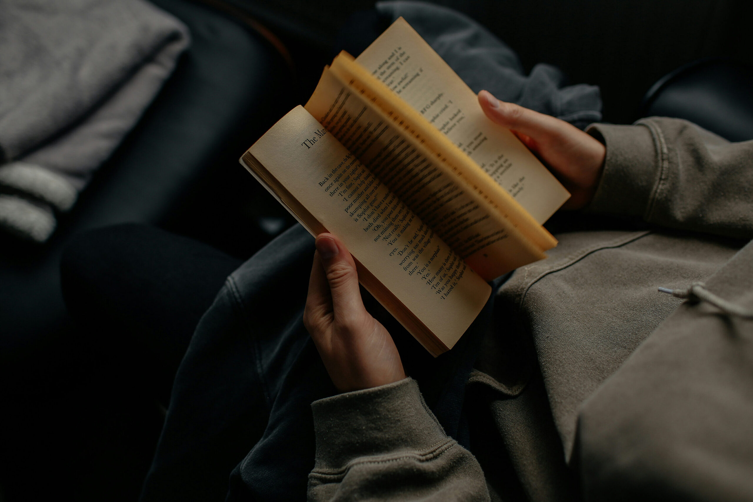 person reading a book open on their lap in low natural light, reading for pleasure