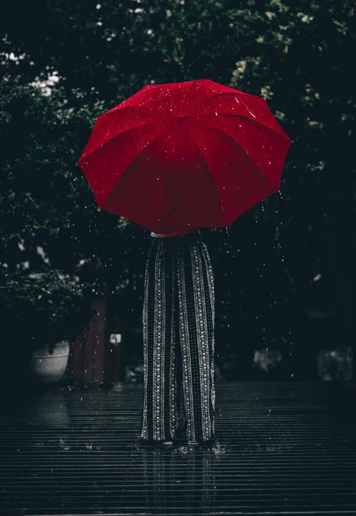 retrato desaturado de día lluvioso con el torso de una persona oculto tras un paraguas rojo