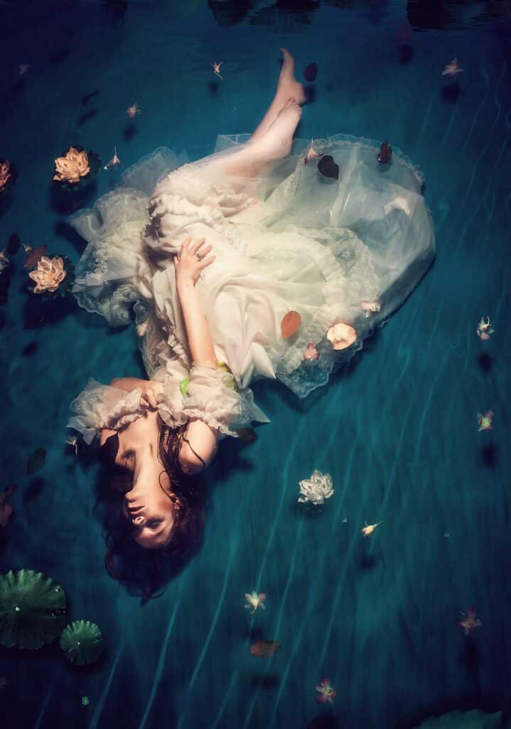 dreamy model posed in white dress laying in water and flowers