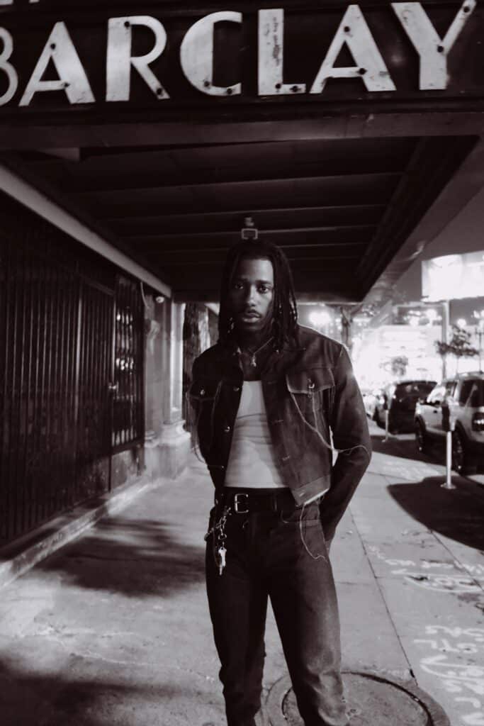 foto editorial en blanco y negro de un hombre negro con trenzas vistiendo vaqueros