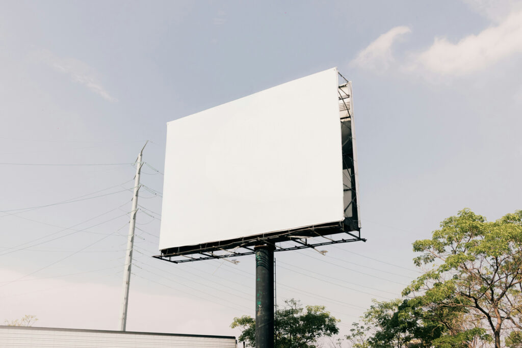 empty white billboard with telephone pole trees and cloudy sky behind it