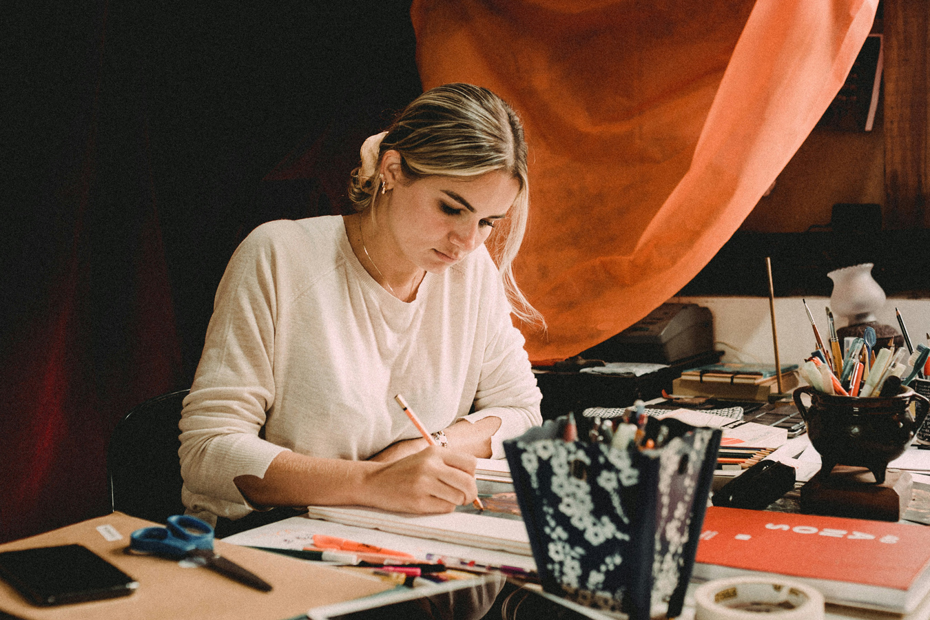 female artist sitting at desk using colored pencils and mixed media