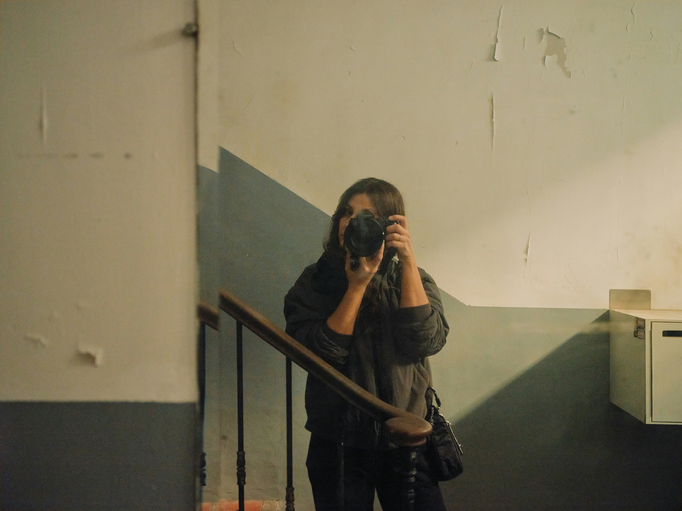 female photographer taking self portrait using a mirror in a dingy stairwell
