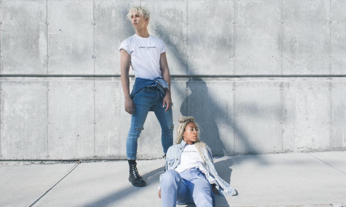 Homem e mulher de camiseta branca e jeans azul contra uma simples parede de concreto cinza