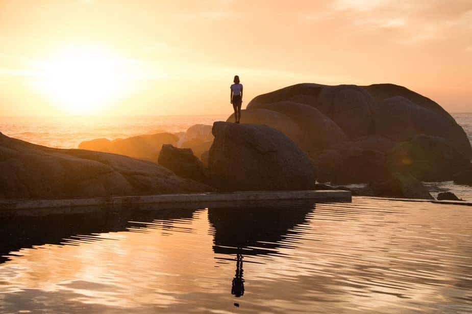 chica al atardecer sobre unas rocas en el agua