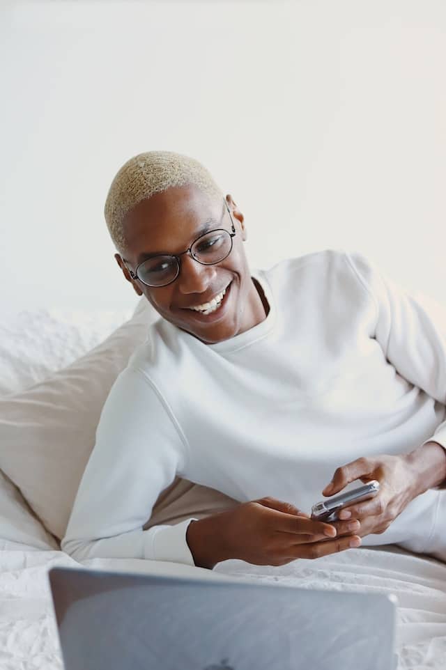 Man smiling holding a phone and looking at a laptop