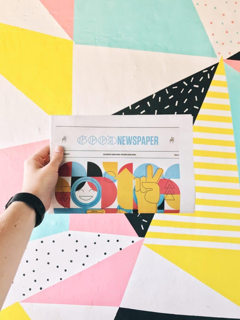 hand holding a cheerful designed newspaper in front of a patterned wall