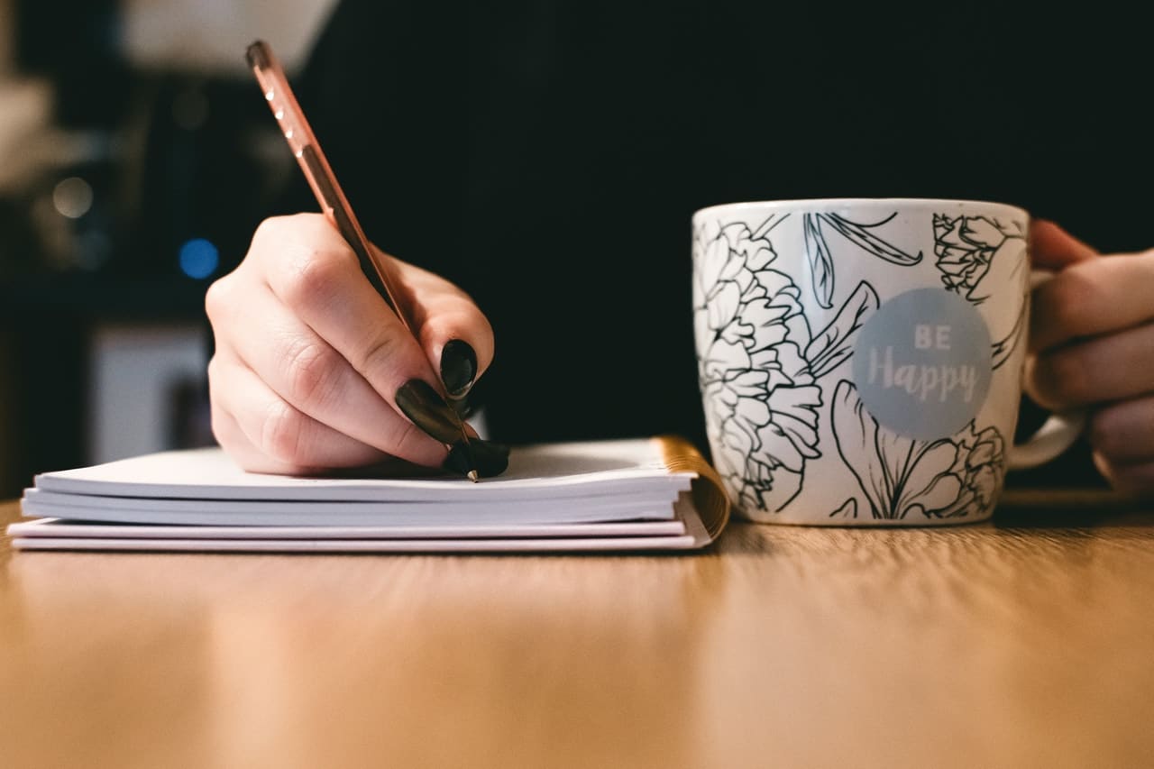 mano_escribiendo_y_sosteniendo_taza_azul