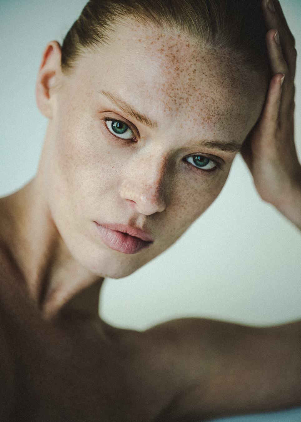 Close-up portrait of a freckled woman with green eyes, hand resting on her head. headshot of Veronika Novikova by Alexander Karlov