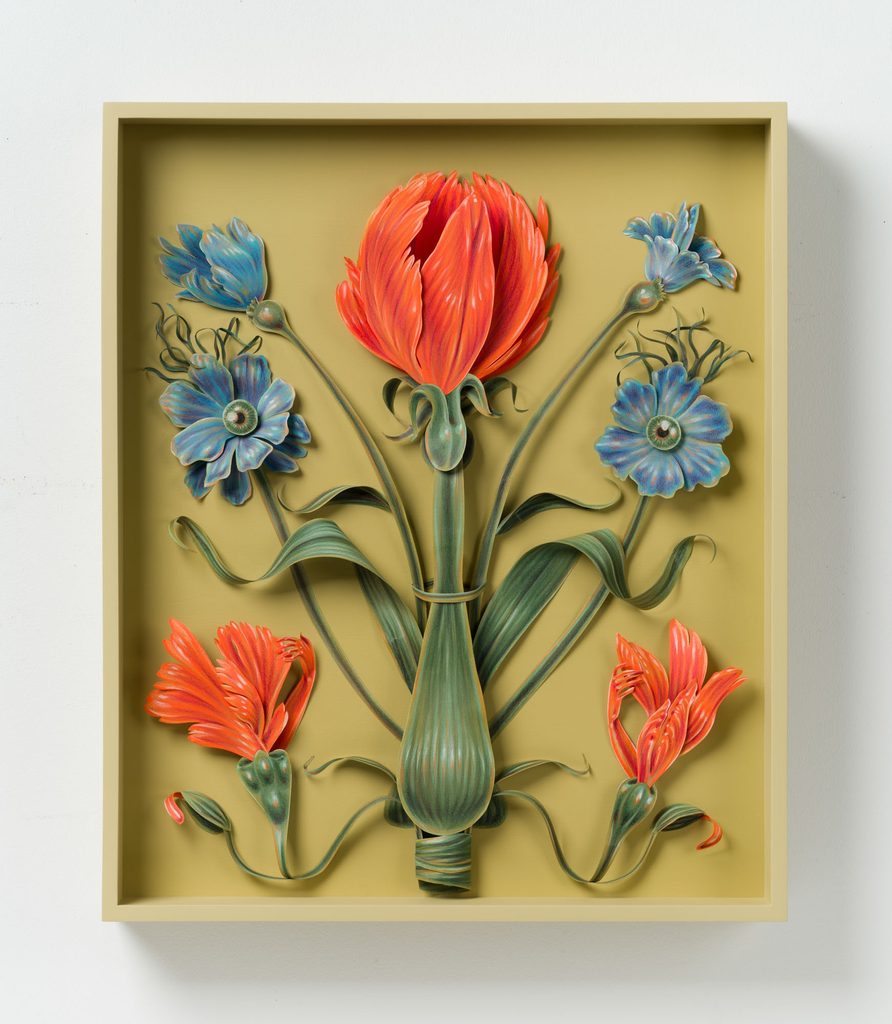 A three-dimensional paper sculpture of a symmetrical floral arrangement features a large orange tulip-like flower in the center flanked by blue blossoms with eye-like centers and smaller orange flowers at the bottom, all set within a shadow box frame.
