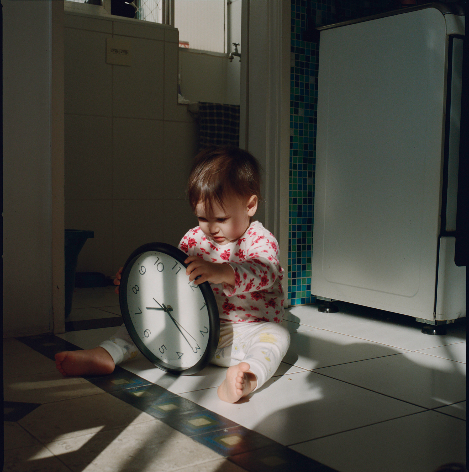 Toddler holding a wall clock in a sunlit kitchen