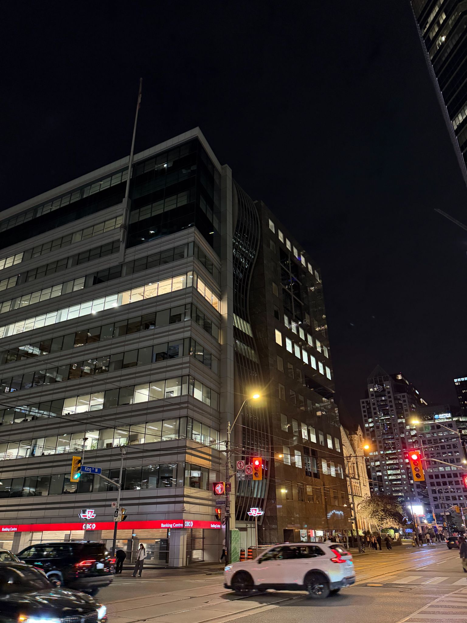 Office buildings, CIBC branch, traffic lights, and cars at King Street West in Toronto at night.