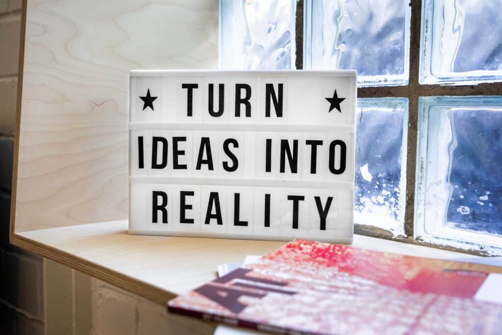 un cartel con una cita que dice "Convierte las ideas en realidad" colocado en una estantería junto a la ventana