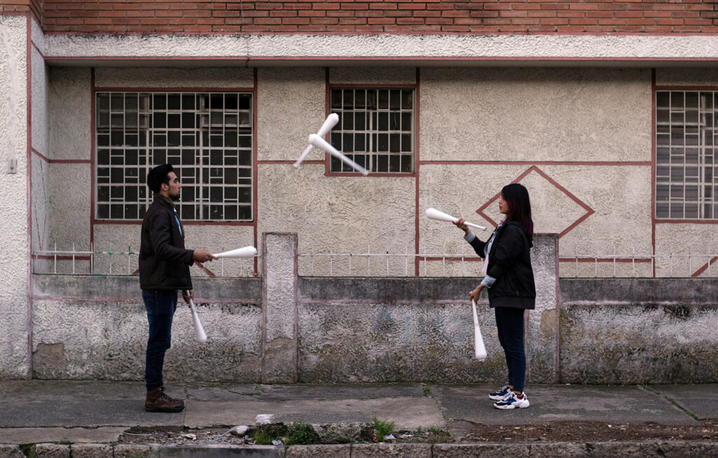 man and woman facing each other on sidewalk juggling with white bats