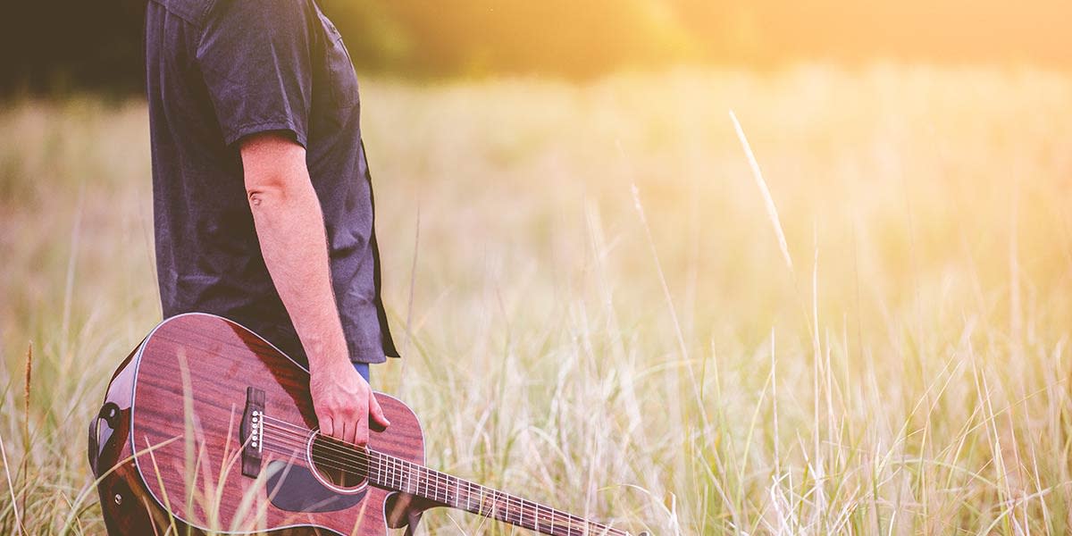 homme-avec-une-guitare-dans-un-champ-d'herbe-ensoleillé