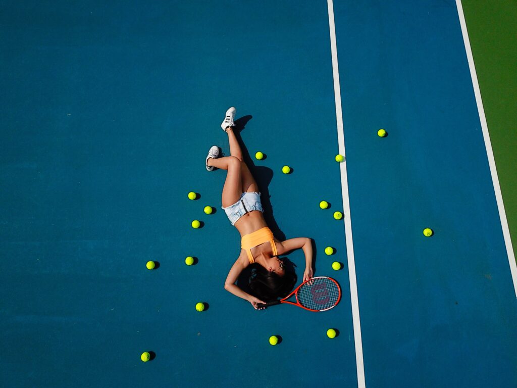 model laying on tennis court surrounded by yellow tennis balls